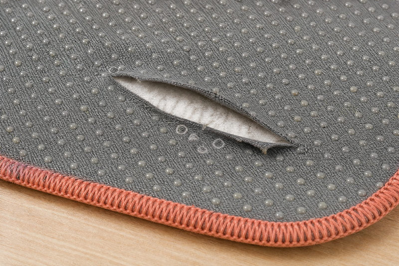 Close-up of the grey silicone-dot underside of a worn washable pee pad, one finger-length split lifting to show the white core, the overlocked edge beside it