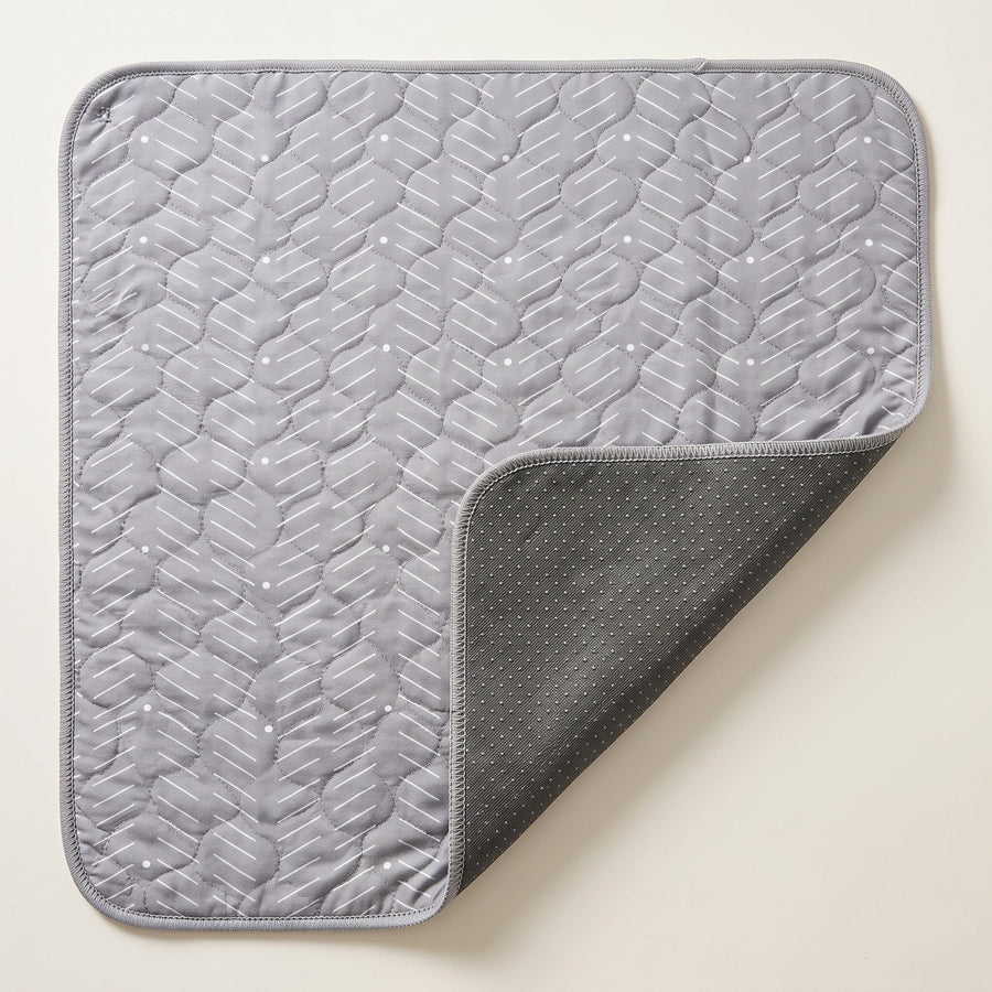 Grey washable pee pad, one corner turned back to show the silicone-dot underside