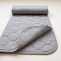 Guinea Pig Grey washable pee pad, plain grey with a large honeycomb quilt, rolled at one end with a corner turned to show the grey underside and its silicone dots