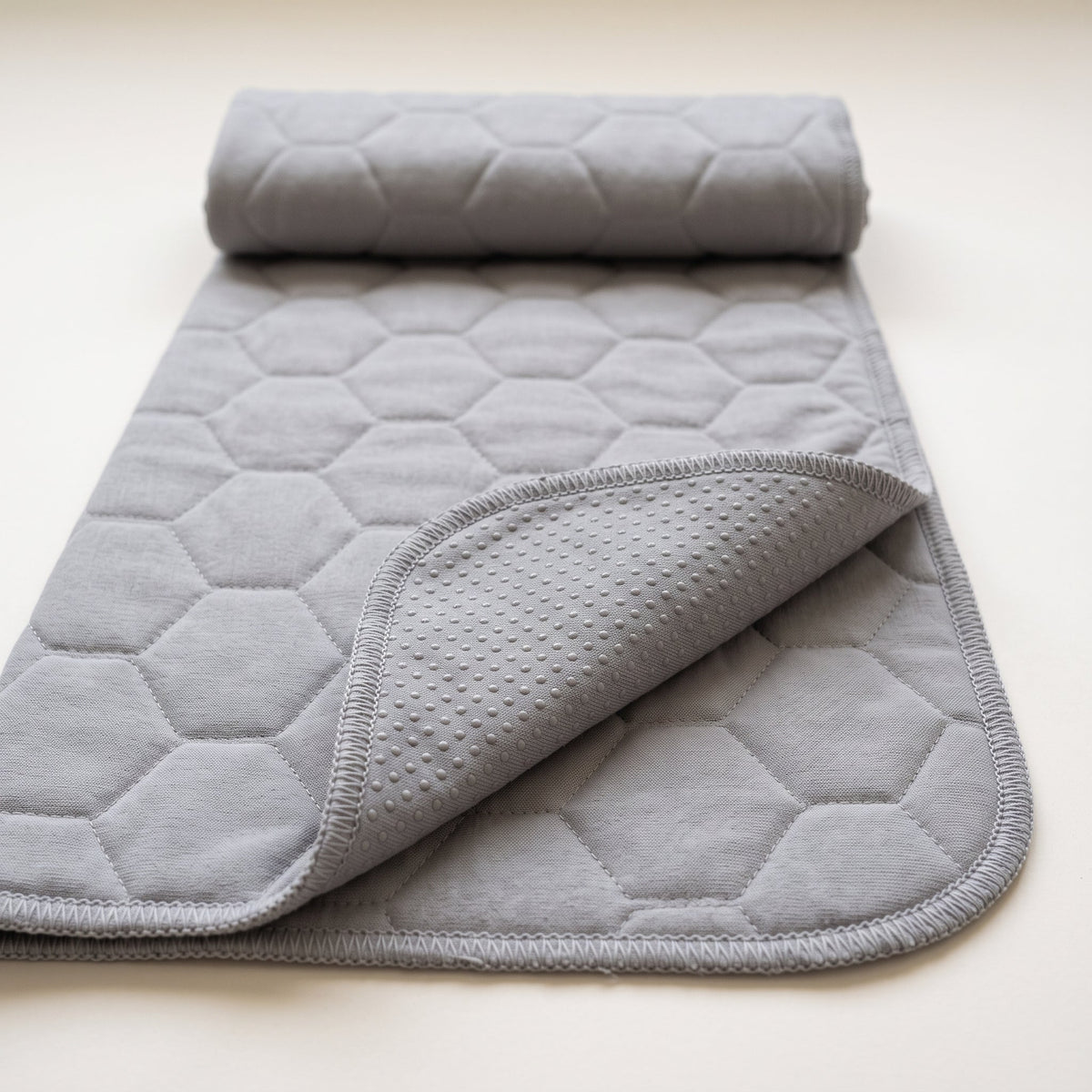 Guinea Pig Grey washable pee pad, plain grey with a large honeycomb quilt, rolled at one end with a corner turned to show the grey underside and its silicone dots
