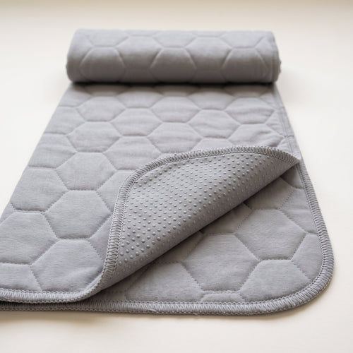 Guinea Pig Grey washable pee pad, plain grey with a large honeycomb quilt, rolled at one end with a corner turned to show the grey underside and its silicone dots