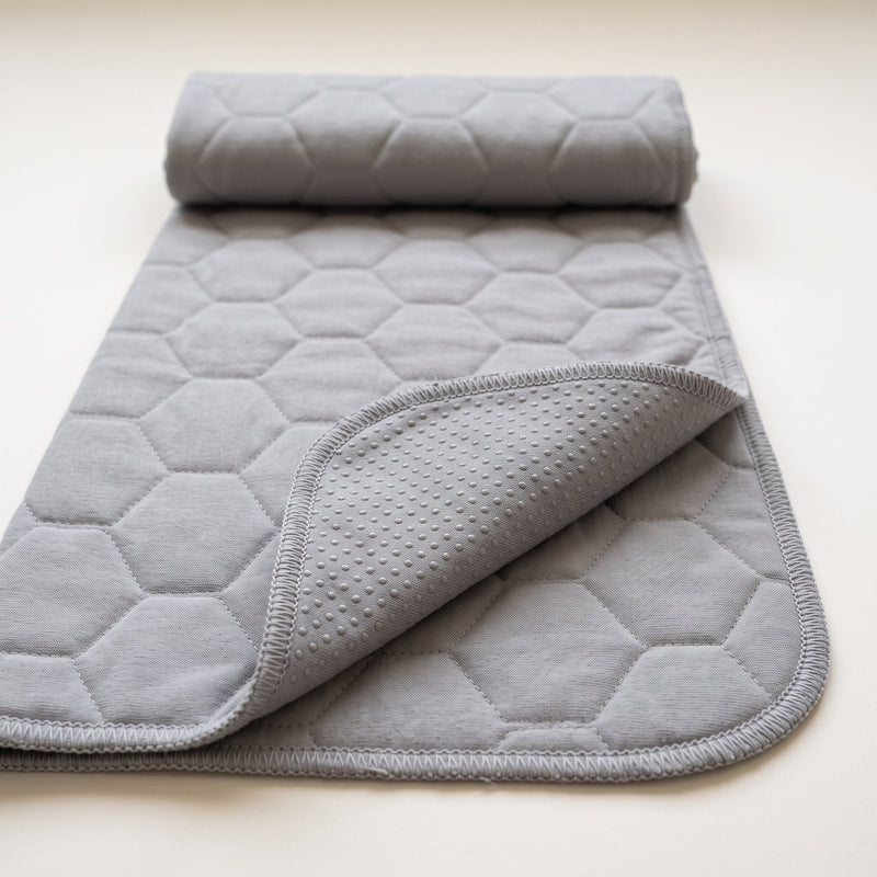 Guinea Pig Grey washable pee pad, plain grey with a large honeycomb quilt, rolled at one end with a corner turned to show the grey underside and its silicone dots