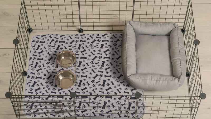 A real customer photo: a wire playpen from above, the pad lining its floor with two bowls and a grey bed on it