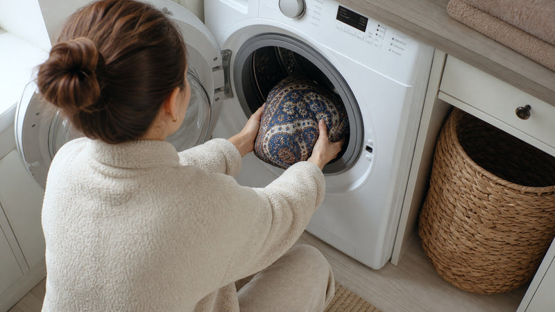 A washable pee pad being fed into a front-loading washing machine, bundled to about the size of a folded bath towel