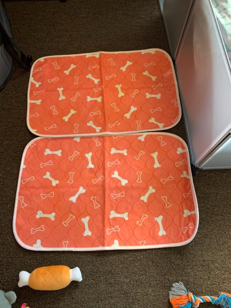 Two of The Proper Pet's orange bones-print washable pads laid flat on the floor